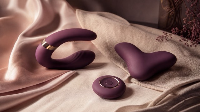A wearable vibrator and its compact remote arranged on folded blush fabric in a tasteful bedroom setting