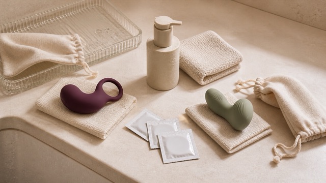 Two pleasure products on separate cloths beside blank barrier packets, cleaner, pouches and a glass tray